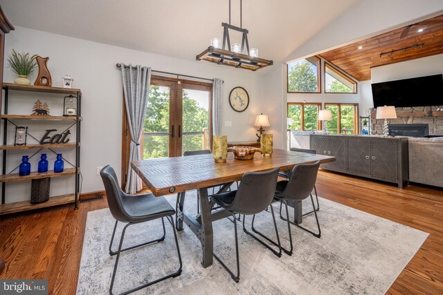 dining room featuring vaulted ceiling, a fireplace, french doors, and hardwood / wood-style floors