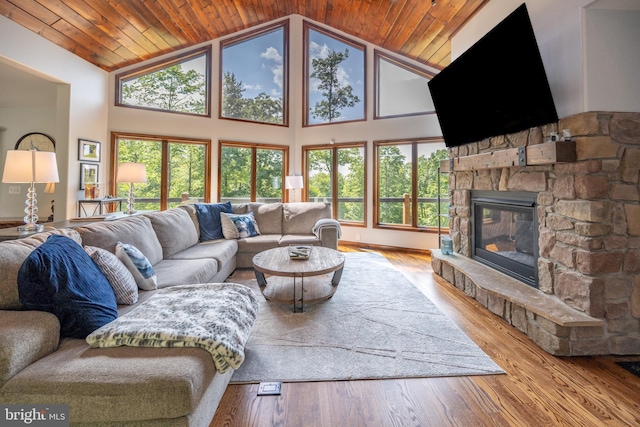 living room featuring a stone fireplace, light hardwood / wood-style floors, a healthy amount of sunlight, and wood ceiling