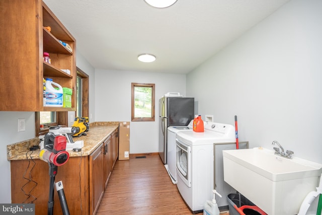 clothes washing area featuring cabinets, hardwood / wood-style flooring, washer and clothes dryer, and sink