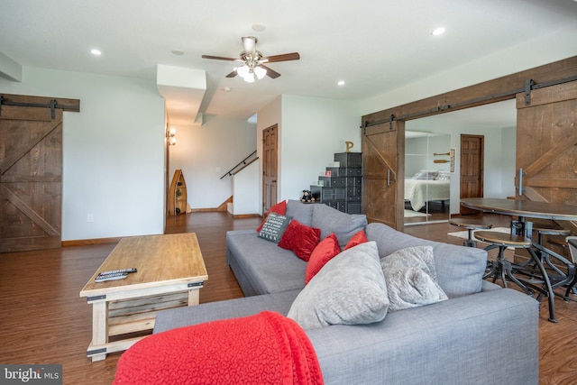 living room with dark wood-type flooring, ceiling fan, and a barn door