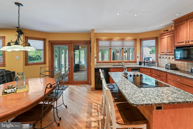 kitchen with light hardwood / wood-style floors, decorative backsplash, light stone counters, black appliances, and a breakfast bar