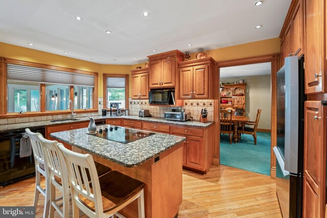 kitchen featuring a center island, stone counters, decorative backsplash, light carpet, and black appliances