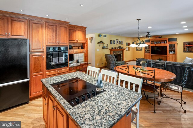 kitchen featuring light hardwood / wood-style floors, decorative backsplash, black appliances, a kitchen island, and a breakfast bar