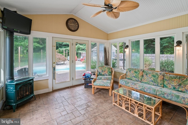 sunroom featuring ceiling fan, vaulted ceiling, a wood stove, and a healthy amount of sunlight