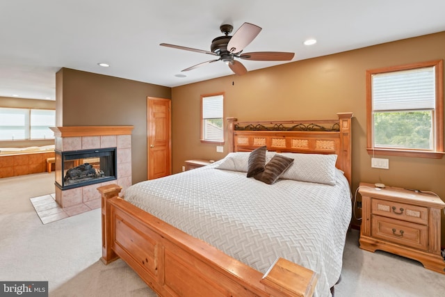 carpeted bedroom featuring ceiling fan, a tile fireplace, and multiple windows