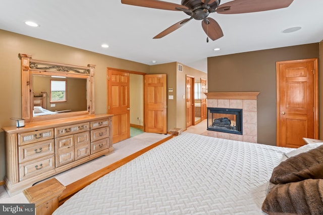 carpeted bedroom with ceiling fan and a tile fireplace