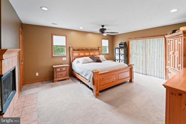 bedroom featuring ceiling fan, a tiled fireplace, multiple windows, and light carpet