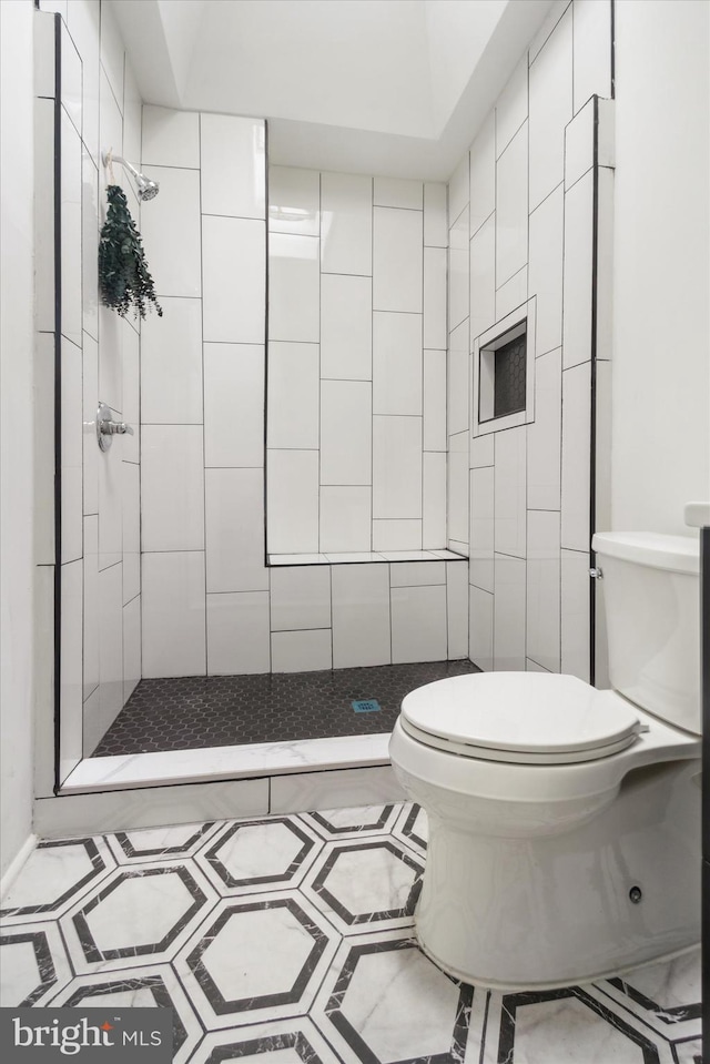 bathroom with a tile shower, tile patterned floors, and toilet