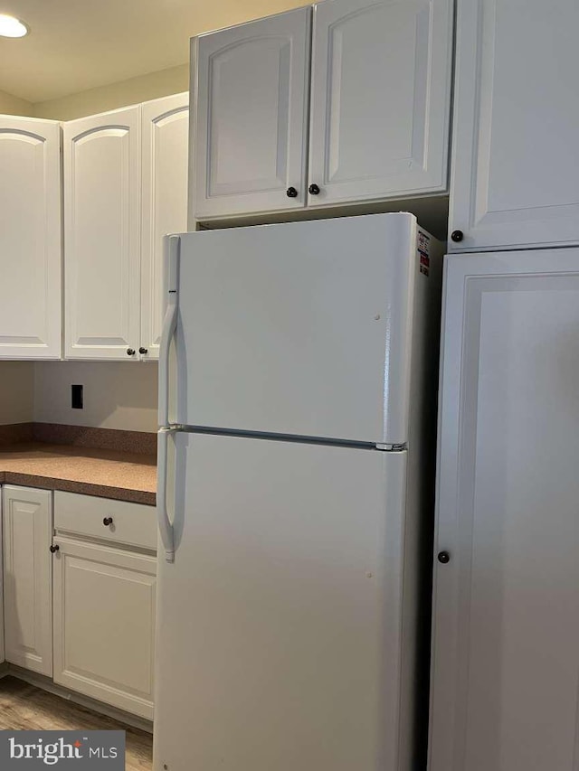 kitchen with white refrigerator, white cabinetry, and hardwood / wood-style flooring