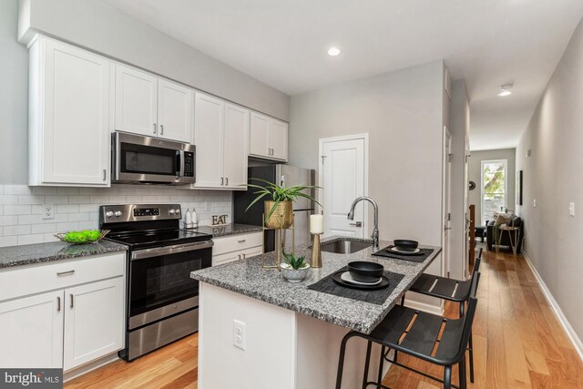 kitchen featuring light hardwood / wood-style flooring, appliances with stainless steel finishes, dark stone countertops, and a kitchen island with sink