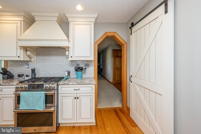 kitchen featuring premium range hood, light stone counters, a barn door, light hardwood / wood-style floors, and range with two ovens