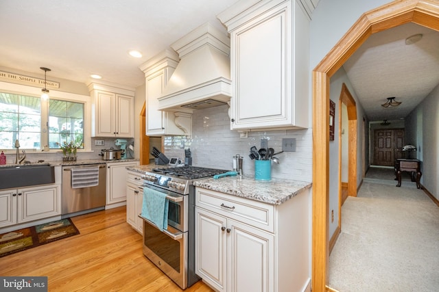 kitchen with stainless steel appliances, sink, light wood-type flooring, light stone countertops, and custom exhaust hood