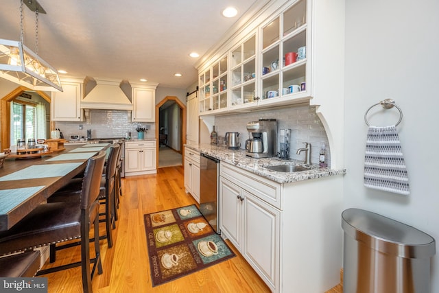 kitchen with light wood-type flooring, custom range hood, tasteful backsplash, and sink