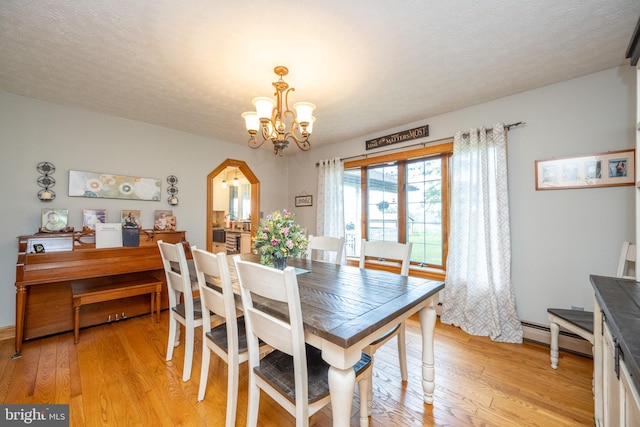 dining space with a baseboard heating unit, a textured ceiling, light hardwood / wood-style flooring, and an inviting chandelier