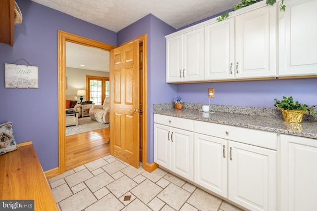 kitchen featuring white cabinets, light hardwood / wood-style floors, light stone counters, and a textured ceiling