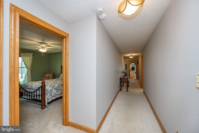 corridor with a textured ceiling and light colored carpet