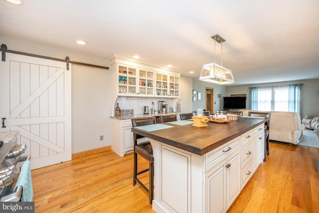 kitchen featuring a breakfast bar area, light hardwood / wood-style flooring, a center island, wood counters, and a barn door