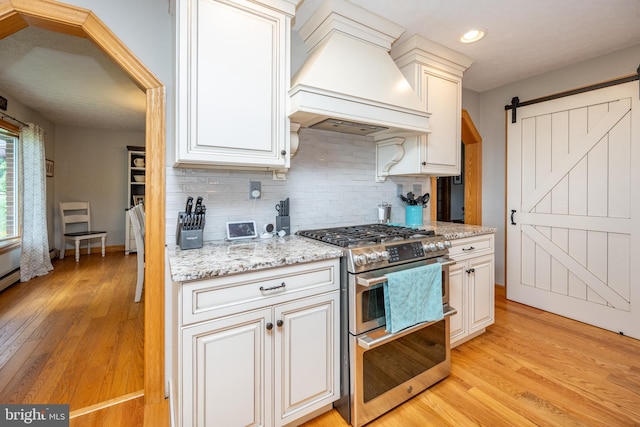 kitchen featuring light wood-type flooring, a barn door, double oven range, custom range hood, and backsplash