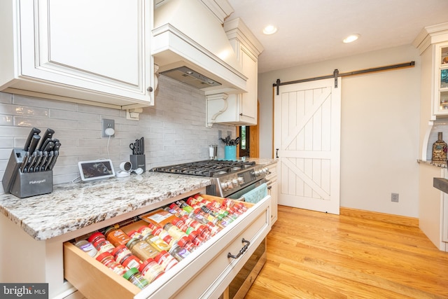 kitchen with backsplash, a barn door, light wood-type flooring, and custom exhaust hood