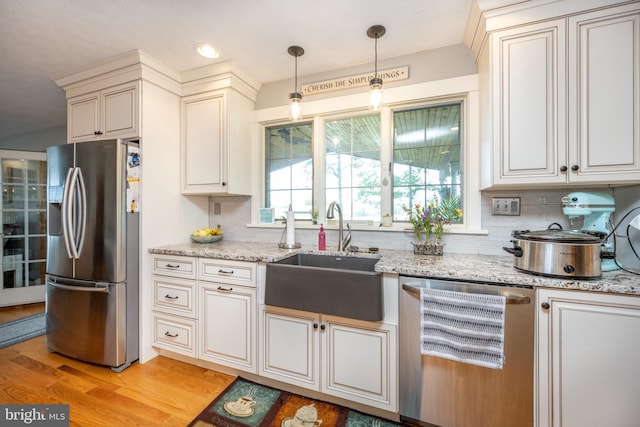 kitchen featuring light hardwood / wood-style flooring, light stone countertops, appliances with stainless steel finishes, decorative backsplash, and sink