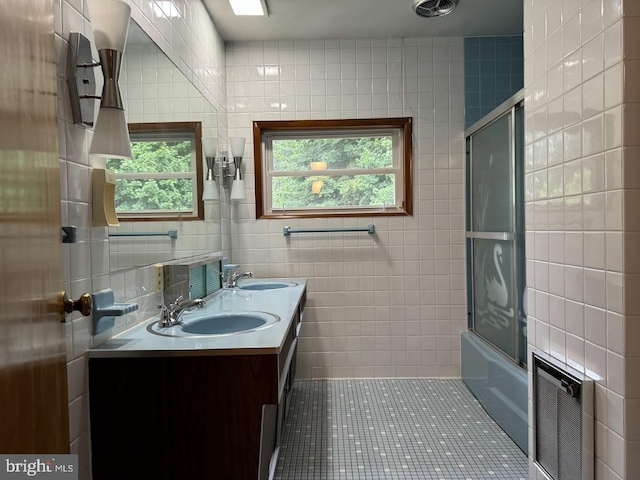 bathroom with tile walls, combined bath / shower with glass door, double sink vanity, and tile patterned floors