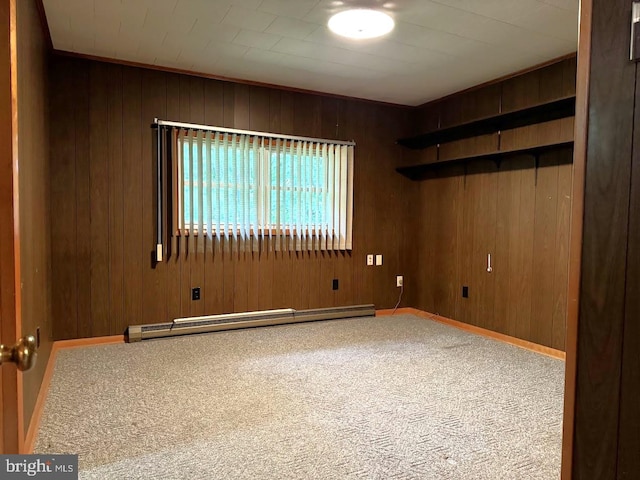 carpeted empty room featuring a baseboard heating unit and wooden walls