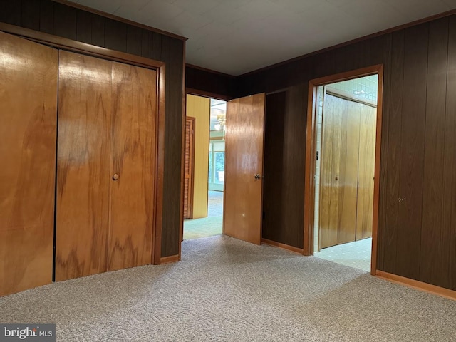 unfurnished bedroom featuring light carpet, wood walls, and a closet