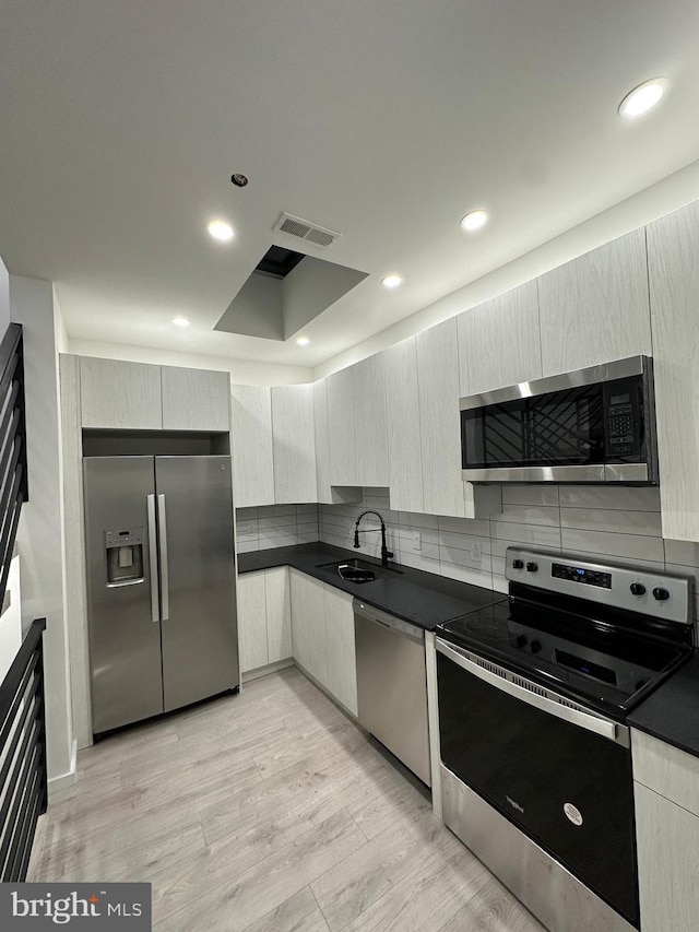 kitchen with decorative backsplash, appliances with stainless steel finishes, sink, and light hardwood / wood-style flooring