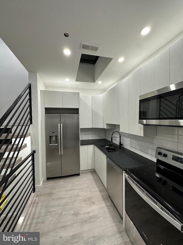 kitchen with appliances with stainless steel finishes, sink, backsplash, a tray ceiling, and light hardwood / wood-style flooring