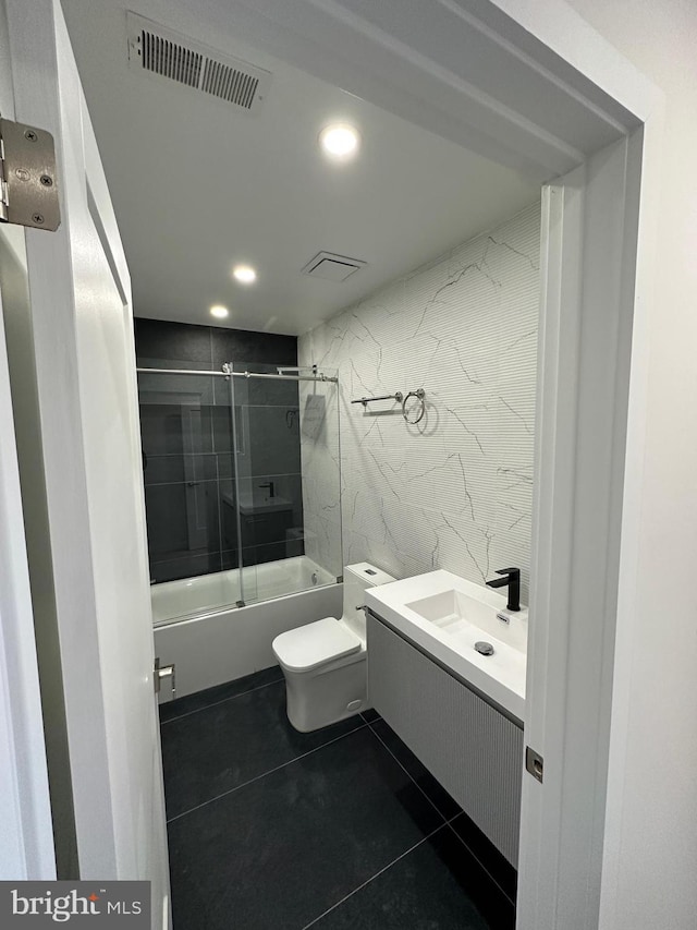 full bathroom with toilet, bath / shower combo with glass door, tile walls, vanity, and tile patterned flooring