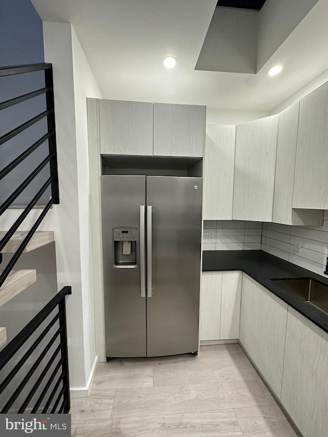 kitchen featuring tasteful backsplash, stainless steel refrigerator with ice dispenser, sink, and light hardwood / wood-style flooring