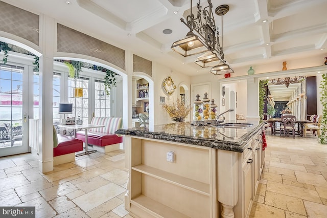 kitchen featuring coffered ceiling, sink, decorative light fixtures, and dark stone countertops