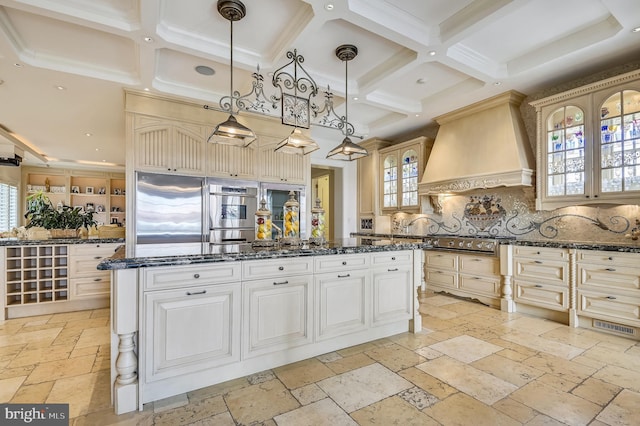 kitchen with appliances with stainless steel finishes, a kitchen island, pendant lighting, dark stone countertops, and custom exhaust hood