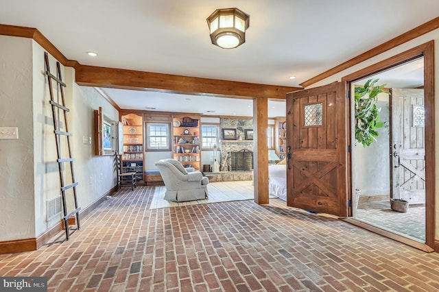 foyer entrance featuring a stone fireplace and ornamental molding