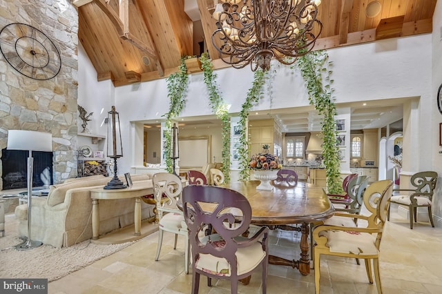 dining area with a stone fireplace, high vaulted ceiling, beamed ceiling, wood ceiling, and an inviting chandelier