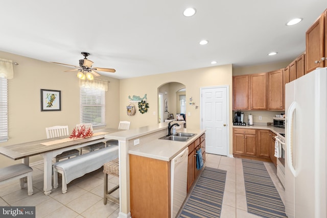 kitchen with sink, a center island with sink, light tile patterned floors, a kitchen breakfast bar, and white appliances