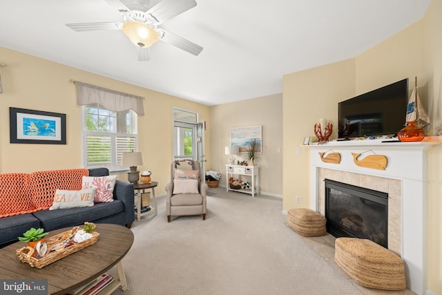 living room featuring ceiling fan, a tile fireplace, and light carpet