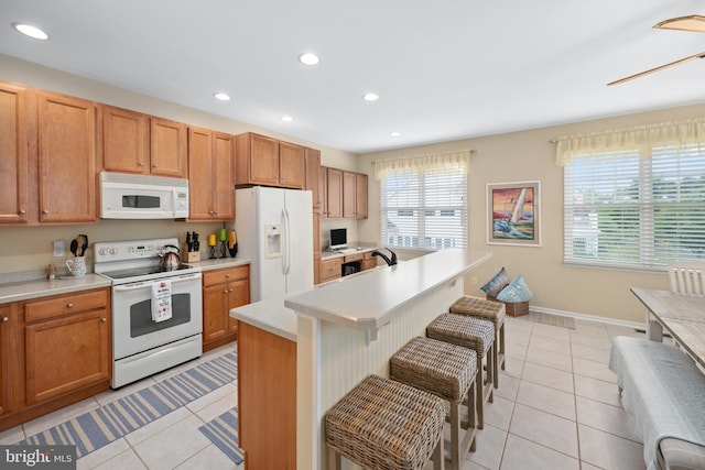 kitchen featuring white appliances, a breakfast bar, ceiling fan, a center island, and light tile patterned flooring