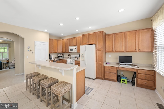 kitchen with a breakfast bar, built in desk, an island with sink, light tile patterned floors, and white appliances