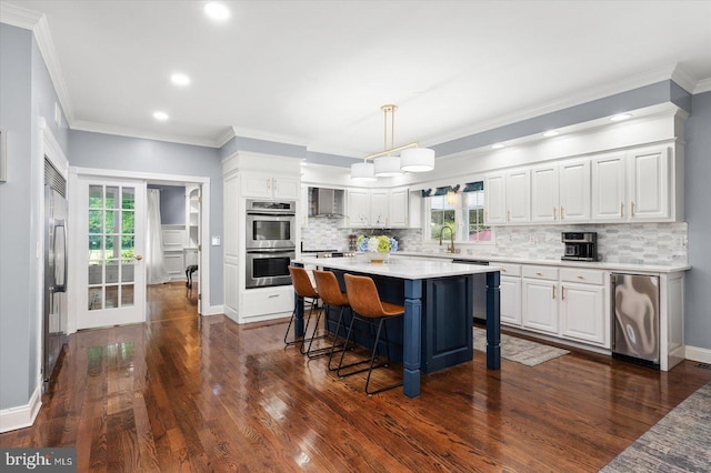 kitchen with wall chimney range hood, refrigerator, double oven, hanging light fixtures, and white cabinets