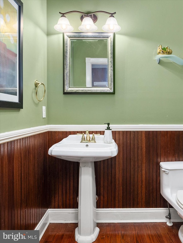 bathroom with wooden walls, wood-type flooring, toilet, and sink