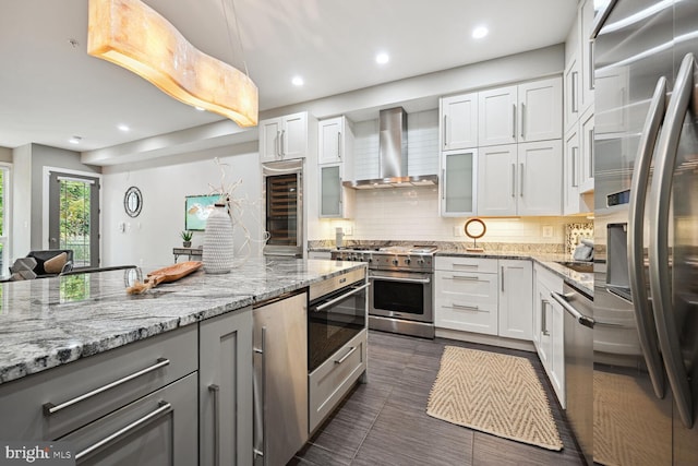 kitchen with wine cooler, wall chimney exhaust hood, white cabinetry, light stone counters, and appliances with stainless steel finishes