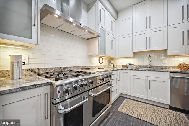 kitchen featuring tasteful backsplash, stone countertops, appliances with stainless steel finishes, wall chimney range hood, and white cabinets