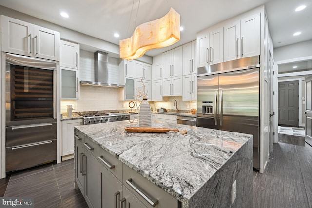 kitchen with stainless steel appliances, a kitchen island, wall chimney range hood, and white cabinets