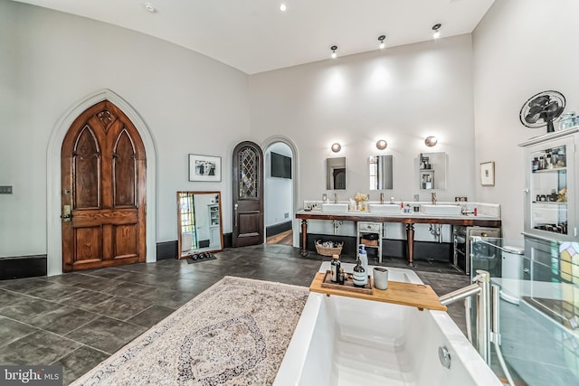 full bath with a washtub, a towering ceiling, and double vanity