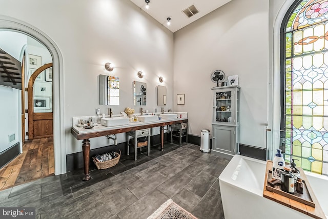 bathroom with a soaking tub, visible vents, a sink, and a towering ceiling