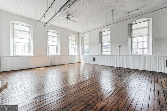 empty room featuring a wainscoted wall, wood-type flooring, a ceiling fan, and plenty of natural light