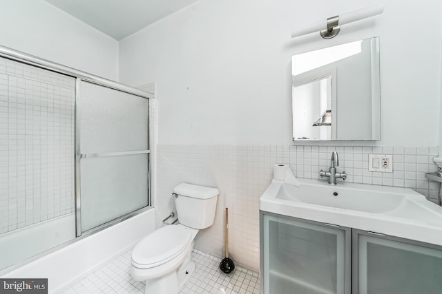 bathroom featuring bath / shower combo with glass door, toilet, a wainscoted wall, tile patterned flooring, and tile walls