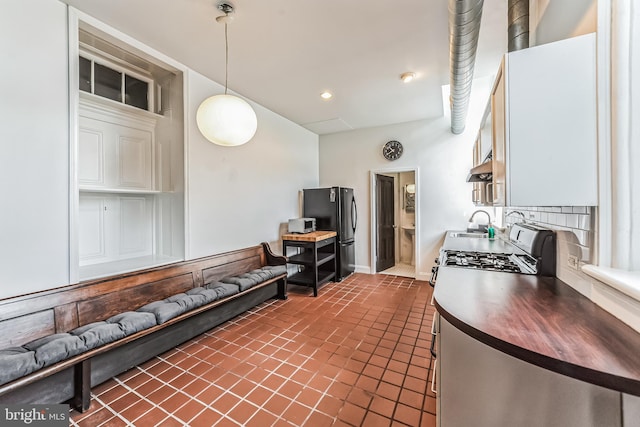 kitchen with white cabinets, stove, freestanding refrigerator, pendant lighting, and backsplash