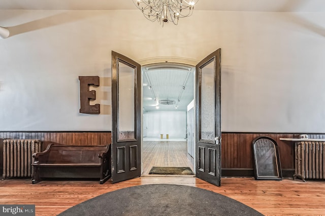 hallway with a notable chandelier, radiator heating unit, hardwood / wood-style floors, and wainscoting